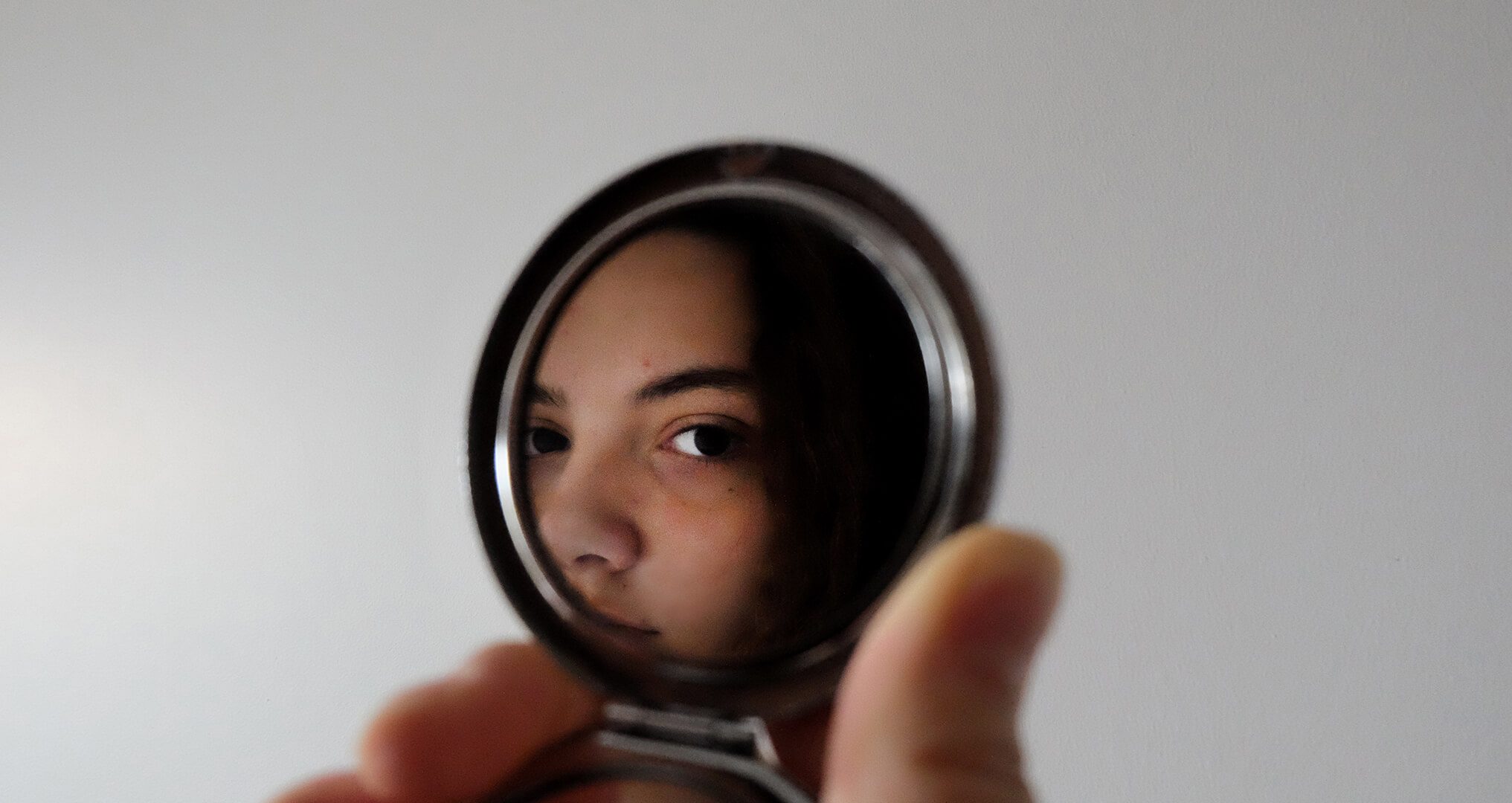 girl holding pcket mirror looking at herself